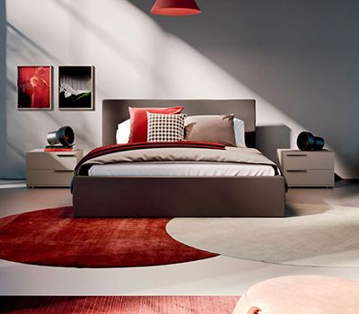 Habitación en tonos moka con dos mesitas de dos cajones. Los textiles como alfombras, nórdico en rojos y beige.