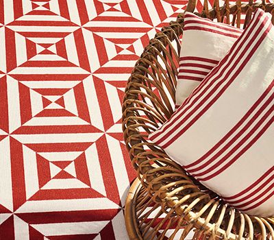 Alfombra de cuadrados con textil de rayas rojas y blancas y silla de mimbre con cojines a juego.